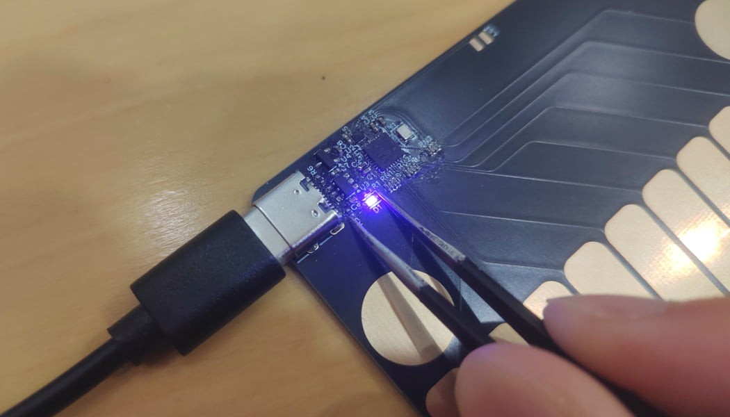 Tweezers shorting the correct pins on the board, while the LED lights up.